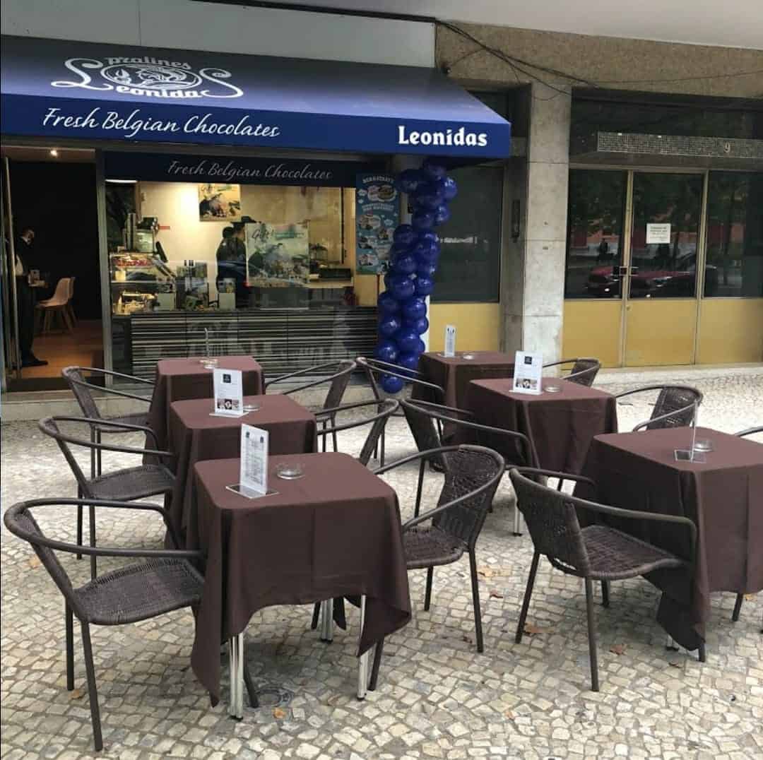 Loja física da Leonidas/ ponto de venda em Portugal em Lisboa Campo Pequeno. Esplanada com cadeiras e mesas em castanho em frente à vitrine da loja.
